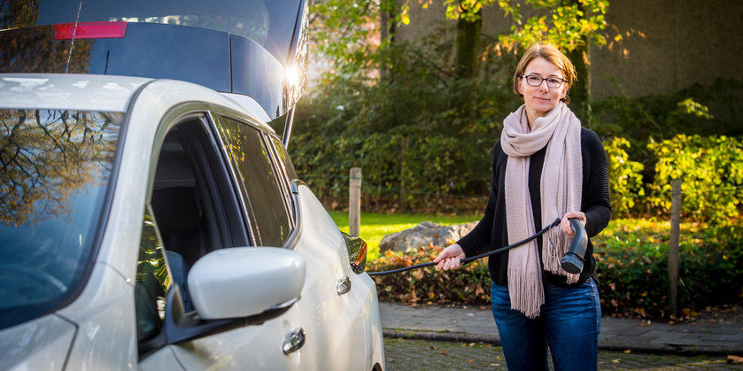 Vrouw staat met laadstekker aan haar elektrische wagen Vrouw staat met laadstekker aan haar elektrische wagen